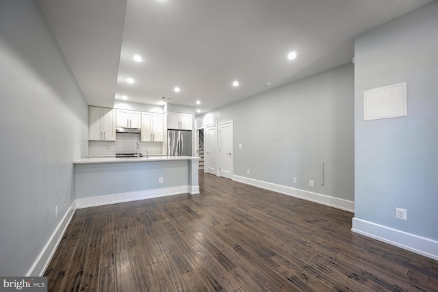 kitchen with kitchen peninsula, backsplash, white cabinetry, stainless steel refrigerator, and dark hardwood / wood-style flooring