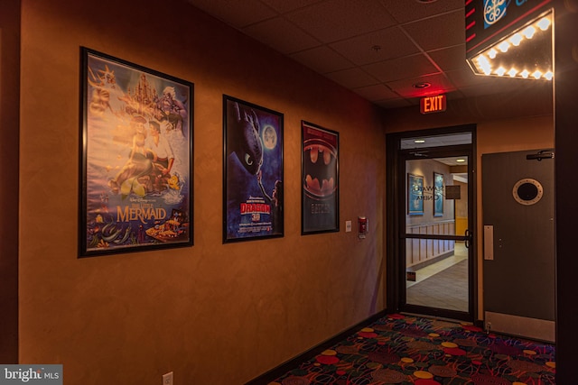 hall with dark colored carpet and a paneled ceiling