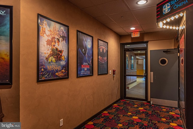 corridor with a paneled ceiling and dark colored carpet