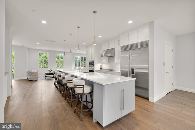 kitchen featuring under cabinet range hood, stainless steel built in fridge, decorative backsplash, light wood-style flooring, and gas cooktop