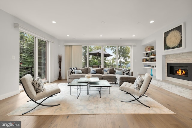 living area featuring a stone fireplace, built in features, plenty of natural light, and light wood finished floors