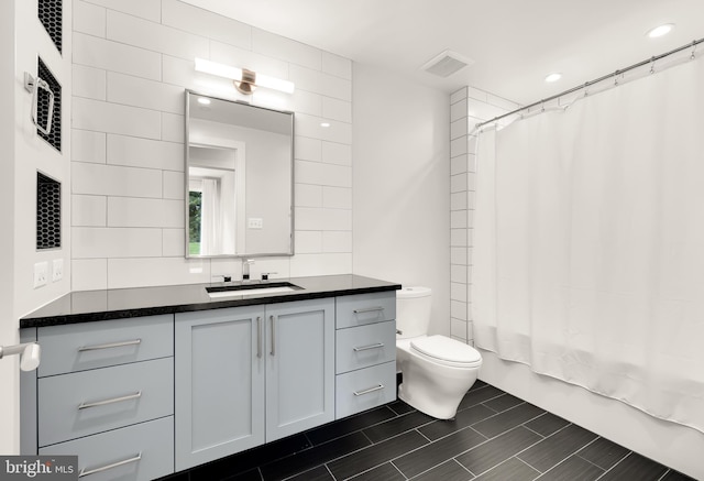 full bathroom with visible vents, toilet, shower / bath combo, tile walls, and vanity