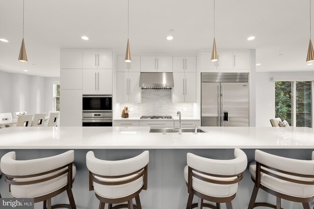 kitchen featuring wall chimney exhaust hood, appliances with stainless steel finishes, a kitchen bar, and sink