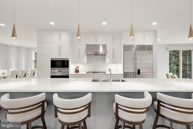 kitchen with a sink, decorative backsplash, white cabinets, under cabinet range hood, and built in appliances