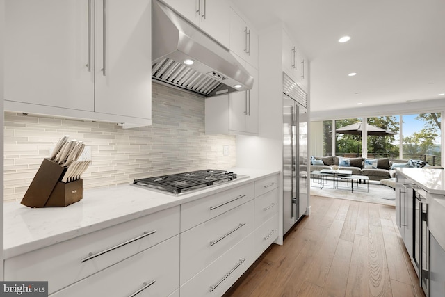 kitchen with light wood finished floors, decorative backsplash, white cabinets, appliances with stainless steel finishes, and under cabinet range hood