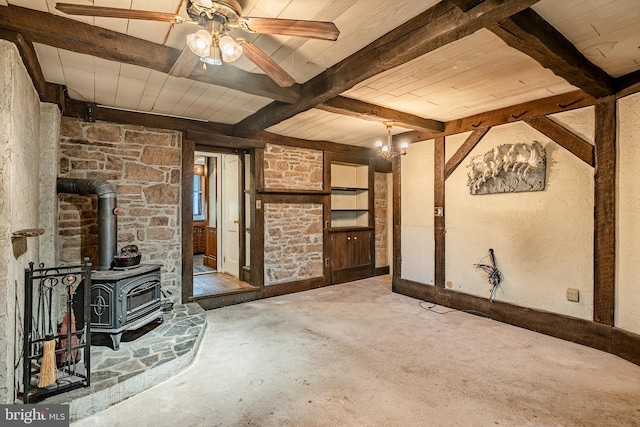 unfurnished living room with ceiling fan, carpet flooring, beam ceiling, and a wood stove