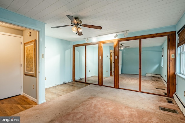 unfurnished bedroom with ceiling fan, multiple closets, light wood-type flooring, and track lighting