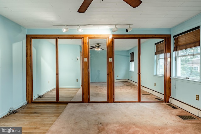 unfurnished bedroom with rail lighting, ceiling fan, light hardwood / wood-style flooring, and multiple closets