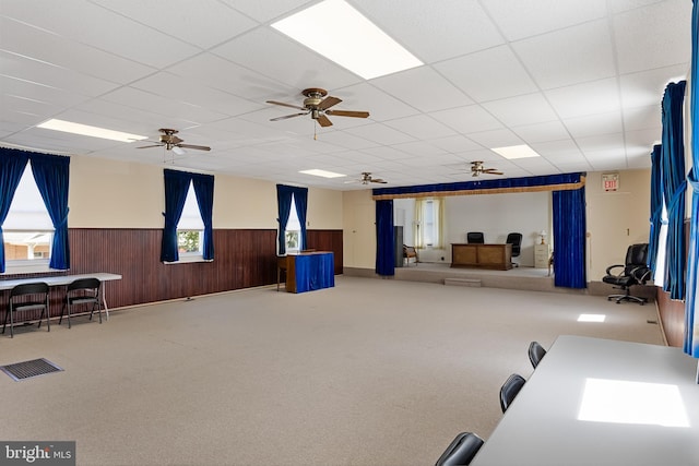 miscellaneous room featuring carpet floors, ceiling fan, wooden walls, and a drop ceiling