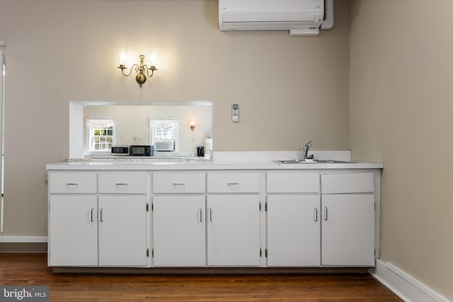 kitchen with dark wood-type flooring, an AC wall unit, sink, and white cabinets