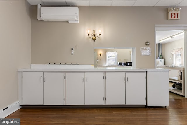 kitchen with dark hardwood / wood-style floors, an AC wall unit, white cabinets, and a drop ceiling