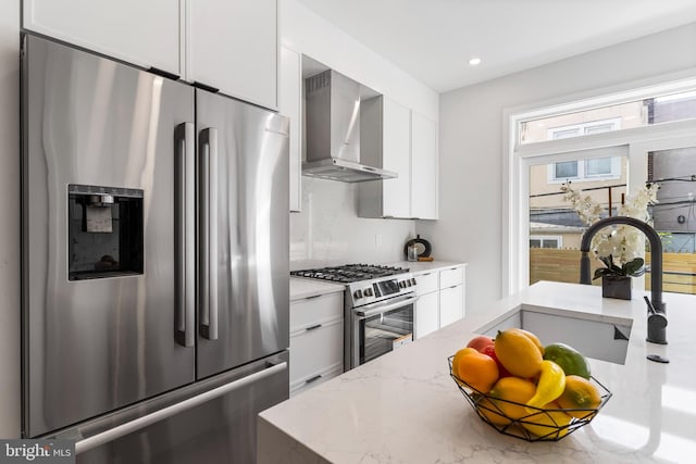 kitchen with stainless steel appliances, sink, light stone countertops, white cabinets, and wall chimney range hood