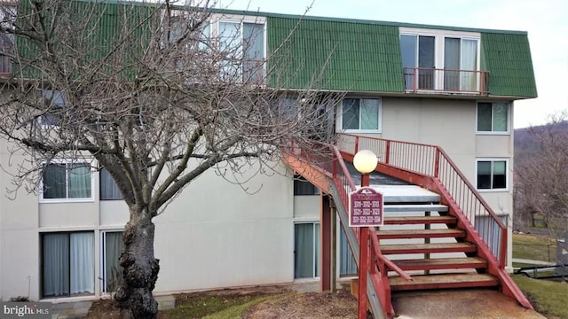 back of property featuring stairway, mansard roof, and stucco siding