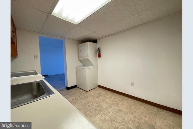 kitchen featuring white cabinets, stacked washing maching and dryer, a drop ceiling, and sink