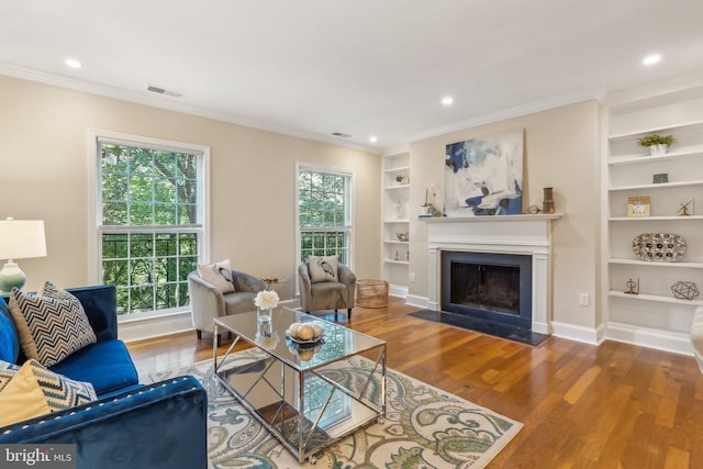 living area featuring built in features, crown molding, visible vents, wood finished floors, and baseboards