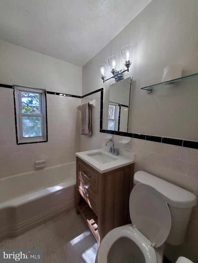 full bathroom featuring tiled shower / bath, vanity, toilet, and tile walls