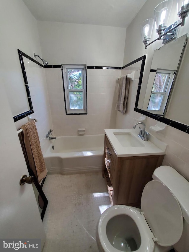 full bathroom featuring tiled shower / bath, vanity, toilet, and tile walls