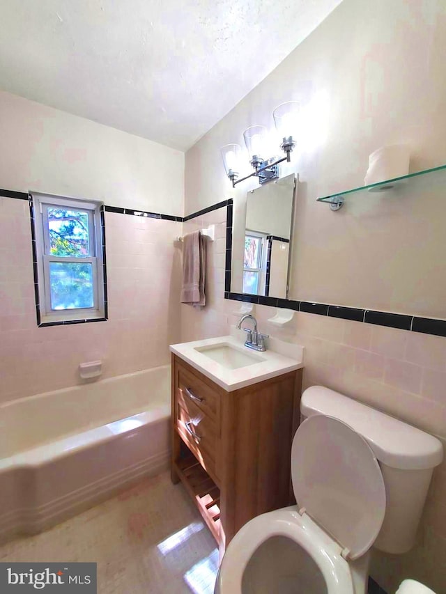 full bathroom featuring tile walls, vanity, tiled shower / bath, and toilet