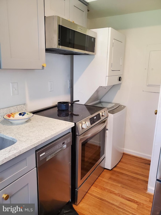 kitchen featuring light wood-type flooring, electric panel, light stone counters, stainless steel appliances, and baseboards