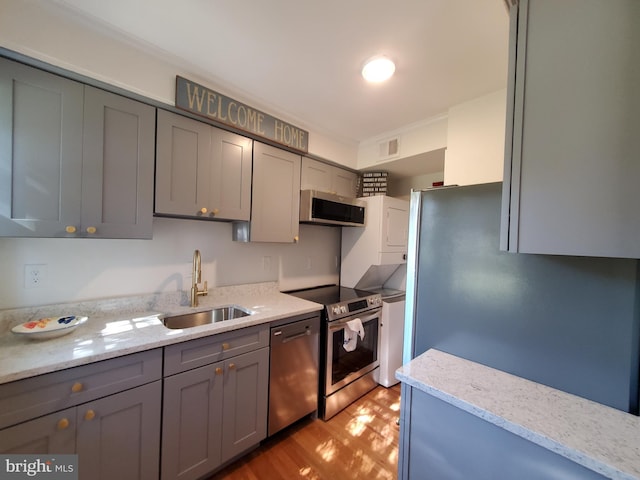 kitchen with light wood-type flooring, light stone counters, a sink, stainless steel appliances, and gray cabinetry