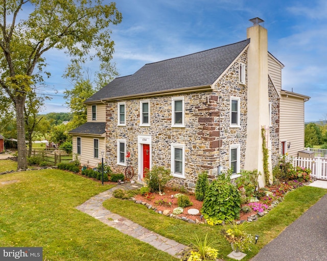 view of front of house with roof with shingles, a chimney, a front lawn, and fence