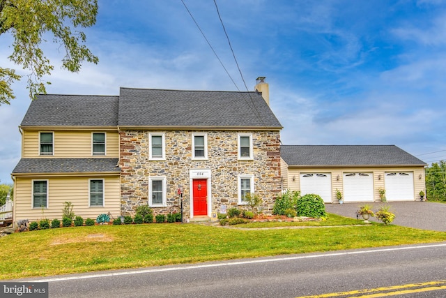 view of front of house featuring driveway, a chimney, a front yard, and a shingled roof