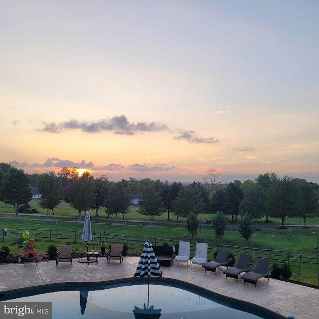 pool at dusk with a patio area and a lawn