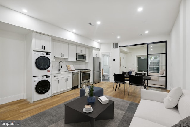 living room with stacked washing maching and dryer, sink, and hardwood / wood-style floors