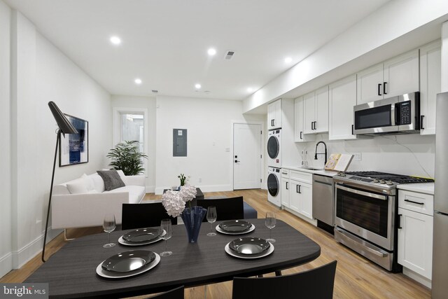 kitchen with appliances with stainless steel finishes, light hardwood / wood-style floors, white cabinetry, sink, and stacked washer / dryer