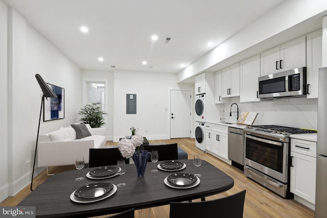 kitchen with stacked washer and clothes dryer, a sink, light wood-style floors, appliances with stainless steel finishes, and light countertops