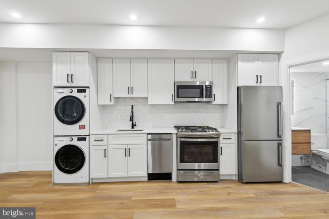 kitchen with stacked washer and clothes dryer, stainless steel appliances, sink, white cabinetry, and light wood-type flooring