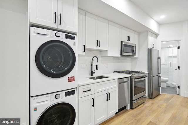 clothes washing area with stacked washing maching and dryer, sink, and light hardwood / wood-style floors