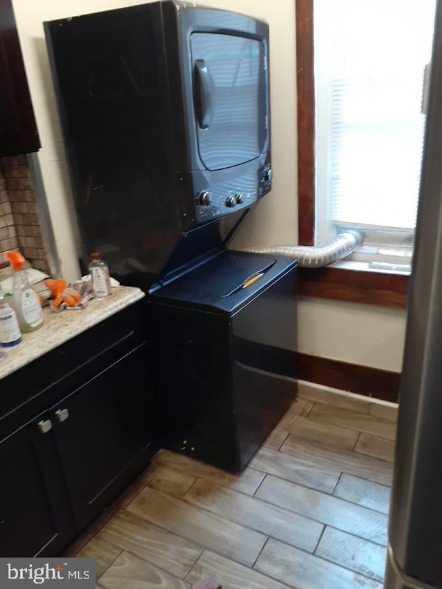 washroom with stacked washer and clothes dryer and light hardwood / wood-style flooring