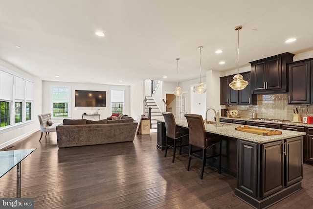 kitchen featuring hanging light fixtures, stainless steel gas cooktop, an island with sink, a breakfast bar, and dark wood-type flooring