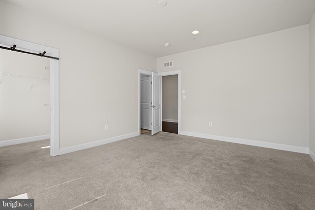 unfurnished bedroom featuring light carpet, a barn door, and a closet