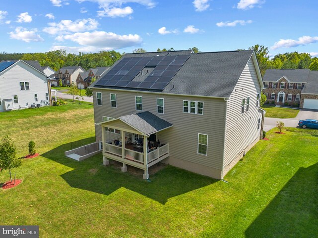 rear view of house featuring a lawn and solar panels