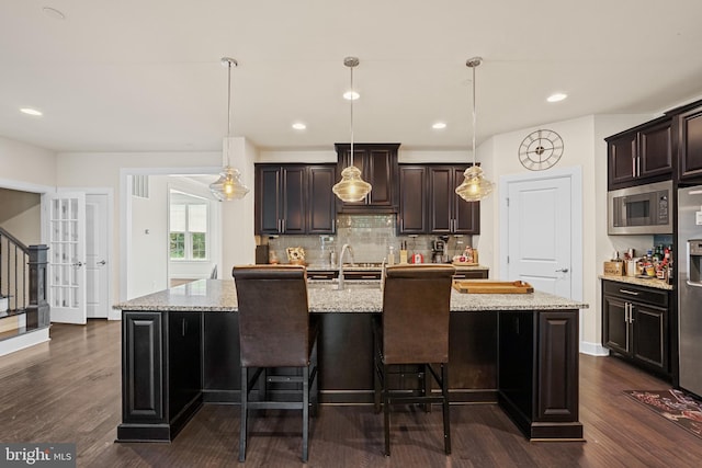 kitchen featuring dark hardwood / wood-style flooring, light stone counters, an island with sink, and stainless steel microwave