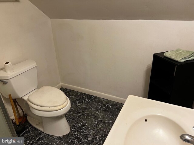 bathroom with toilet, sink, and lofted ceiling