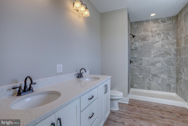 bathroom with wood finished floors, toilet, tiled shower, and a sink