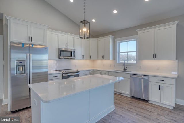 kitchen featuring a sink, vaulted ceiling, appliances with stainless steel finishes, white cabinetry, and a center island