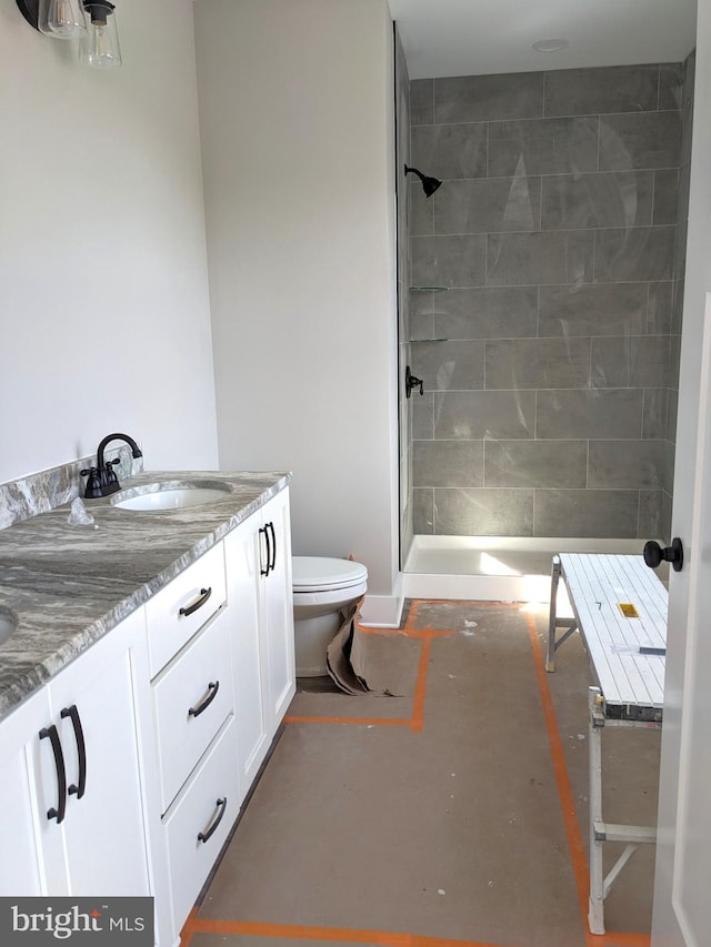 bathroom featuring a tile shower, vanity, and toilet