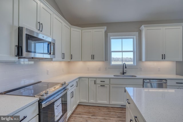 kitchen with a sink, light stone counters, backsplash, white cabinetry, and appliances with stainless steel finishes