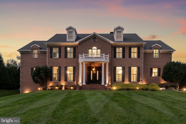 colonial inspired home with a balcony, a lawn, and brick siding