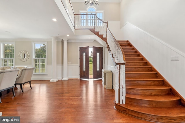 foyer with wood-type flooring, an inviting chandelier, crown molding, and ornate columns