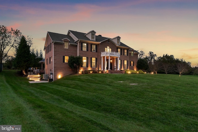 georgian-style home with a front yard, a balcony, cooling unit, and brick siding