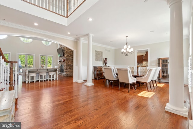 dining space featuring decorative columns, crown molding, hardwood / wood-style flooring, a chandelier, and a high ceiling