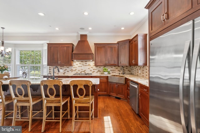 kitchen featuring custom exhaust hood, stainless steel appliances, light stone counters, sink, and an inviting chandelier