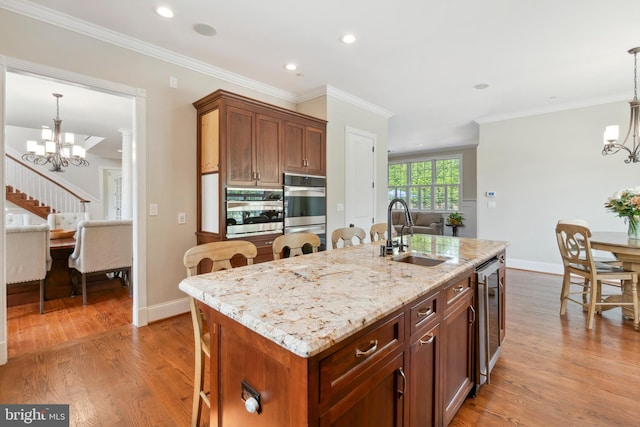 kitchen featuring a kitchen island with sink, pendant lighting, a notable chandelier, light hardwood / wood-style flooring, and sink