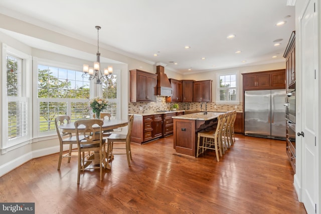 kitchen featuring dark hardwood / wood-style flooring, a center island with sink, custom range hood, appliances with stainless steel finishes, and light stone counters