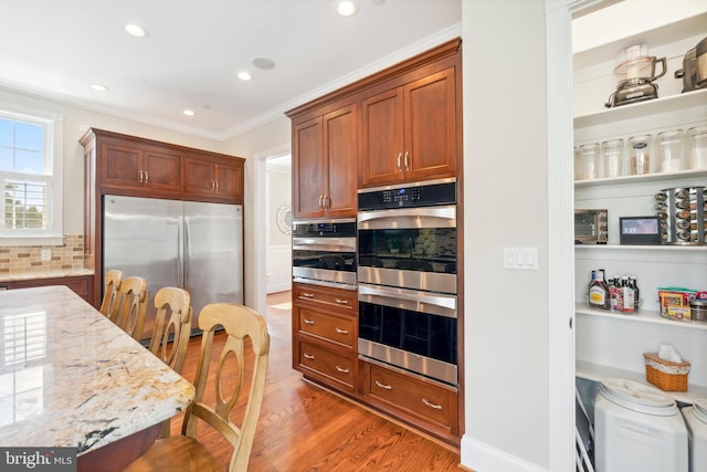 kitchen with wood-type flooring, appliances with stainless steel finishes, ornamental molding, decorative backsplash, and light stone counters